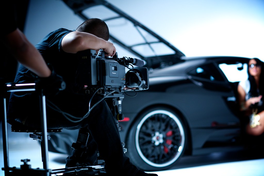 The man in the picture is filming the car with a professional camera for filming